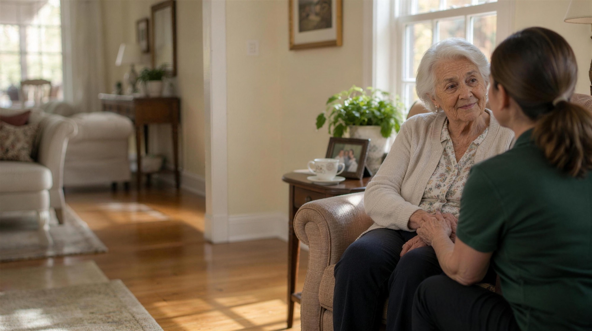 A caregiver holding an older woman's hand in her living room